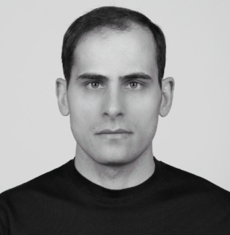 A headshot of Elbert Souza with a neutral facial expression and wearing a black T shirt.